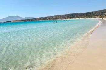 Clear shallow turquoise water along the long sandy curve of Pori beach, Koufonisia